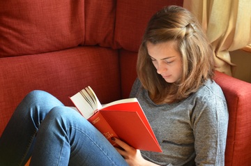 Chica sentada en un sofá leyendo un libro.