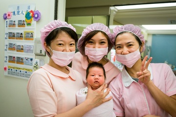 Tres enfermeras posan con un recién nacido.