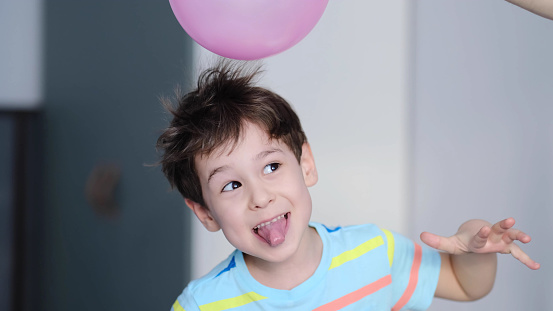 Niño con los pelos de punta que tocan un globo rosa situado encima de su cabeza.