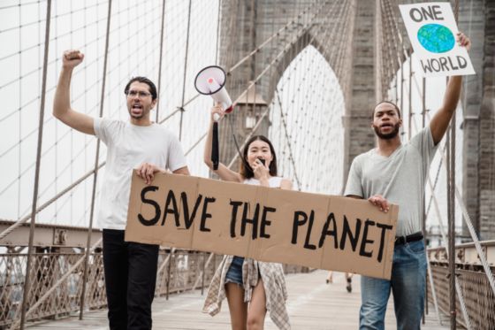 En la fotografía aparecen tres jovenes sobre un puente, llevan un eslogan o cartel en las mano, en el se puede leer 'salvemos el mundo'.