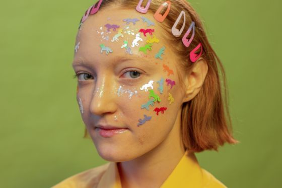 En la fotografía aparece la cara de una adolescente con el pelo corto, en la cara tiene pegado pegatinas de brillantes, animales y formas.