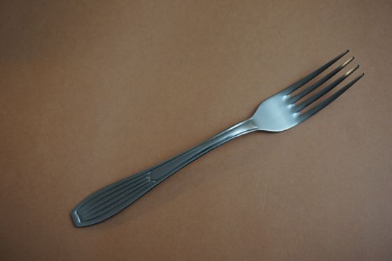 En la fotografía aparece un tenedor de metal sobre un plano de color marrón.