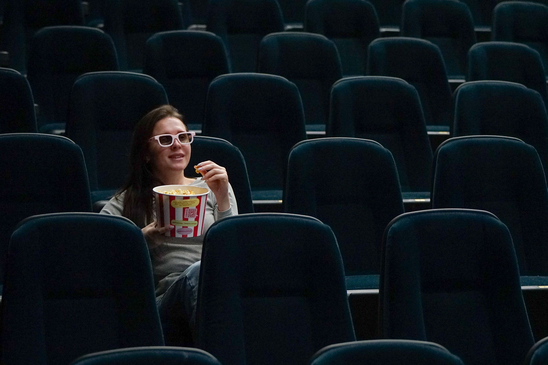 Una sala de cine en la que hay una mujer sentada viendo una película y comiendo palomitas.