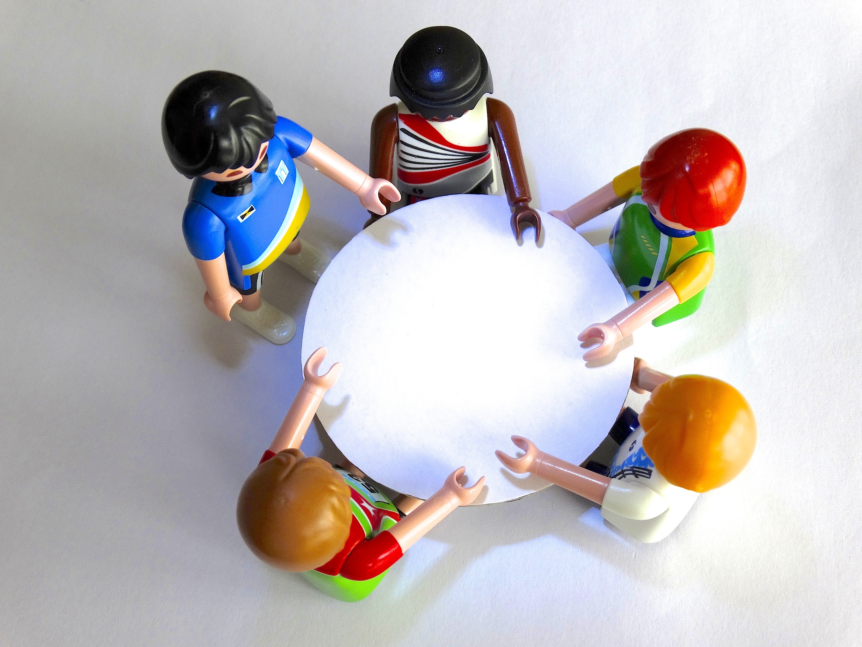 La imagen muestra desde arriba cinco muñecos sentados alrededor de una mesa redonda.