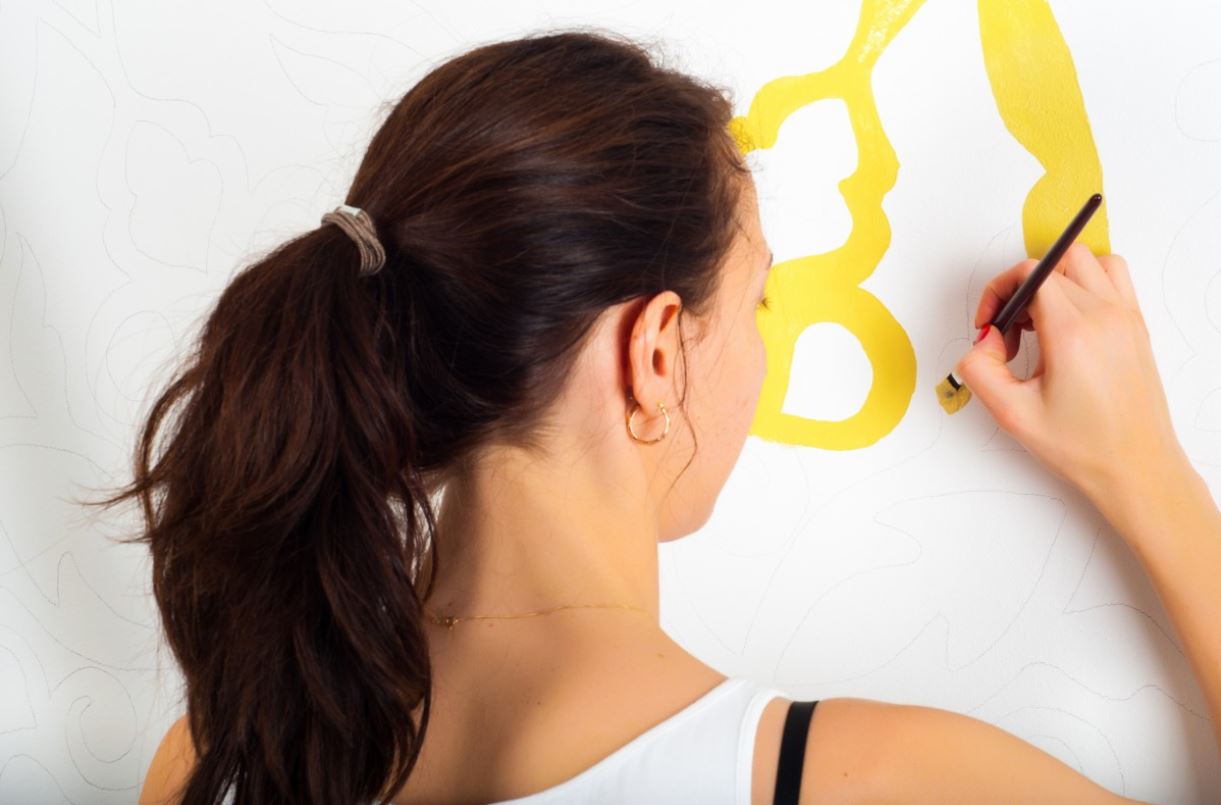 La imagen muestra a una persona de espaldas pintando en la pared con un pincel.