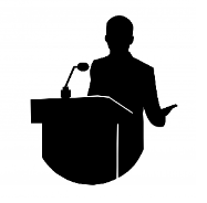 La imagen muestra la silueta de una persona hablando detrás de un atril con un micrófono.