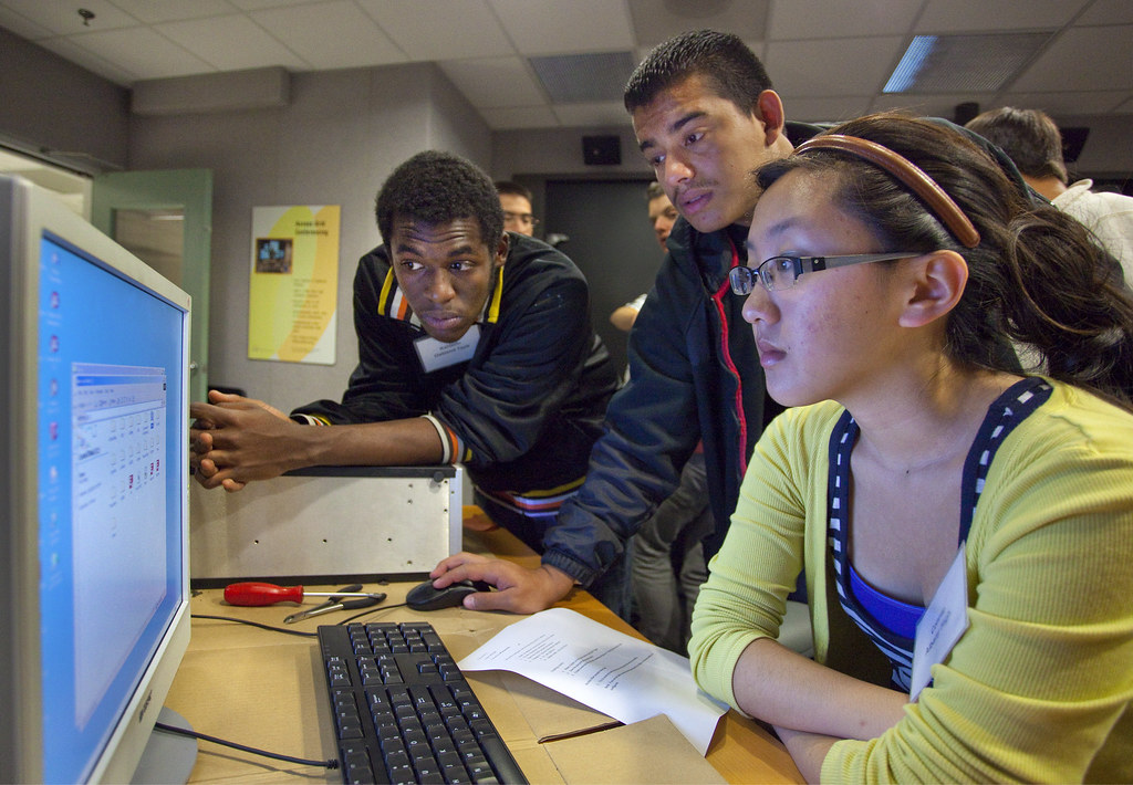 La imagen muestra a tres estudiantes mirando la pantalla de un ordenador.