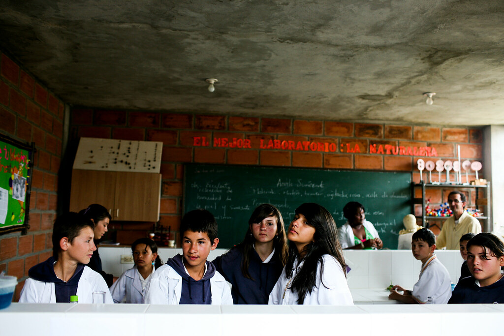 La imagen muestra a un grupo de estudiantes en un aula de ciencias.