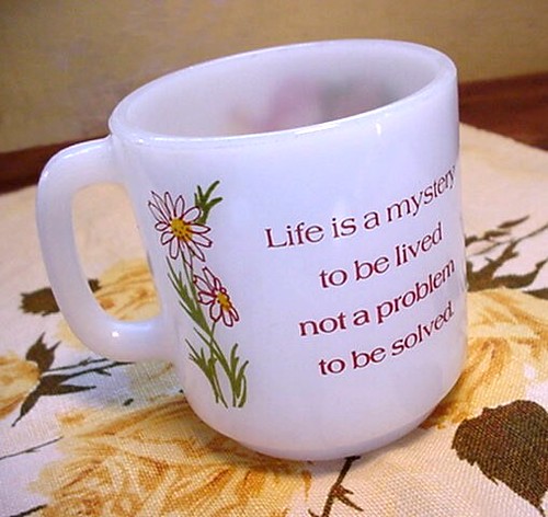 La imagen muestra una taza con un lema impreso Life is a mystery to be lived, not a problem to be solved.