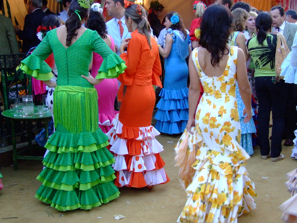 La imagen muestra a varias mujeres de espaldas con trajes de flamenca en la feria.
