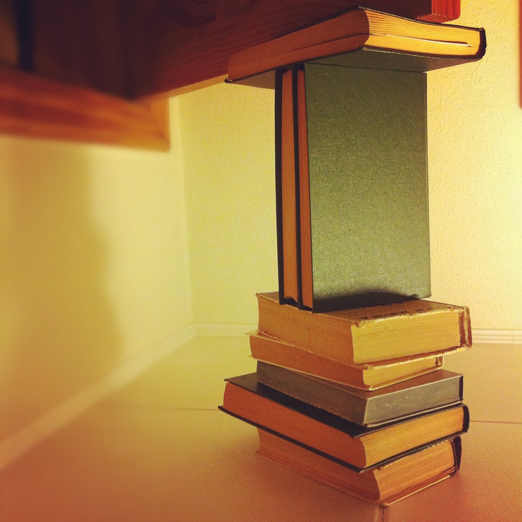 La imagen muestra una columna de libros y uno encima en vertical que apoya a otro en horizontal.