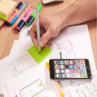 La imagen muestra un escritorio con un móvil, folios y subrayadores, una mano escribe sobre el post-it.