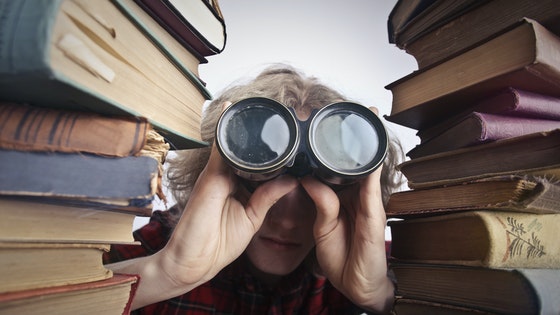  La imagen muestra a un joven con unos prismáticos rodeado de libros 