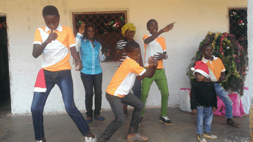 La imagen muestra a un niño africano en el centro de la foto bailando con su familia en una celebración navideña. Aparecen también en la foto su madre, su abuela y sus hermanos mayores y pequeños. 