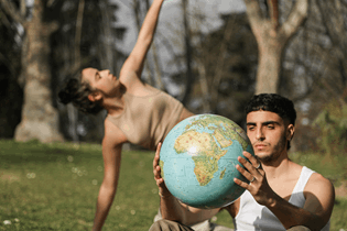 La imagen muestra dos jóvenes, uno de ellos observando un globo terráqueo que sostiene entre las manos, y una chica detrás danzando.