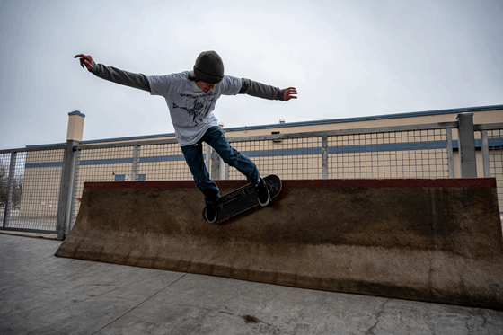 La imagen muestra un adolescente haciendo piruetas con un skate en una pared baja.