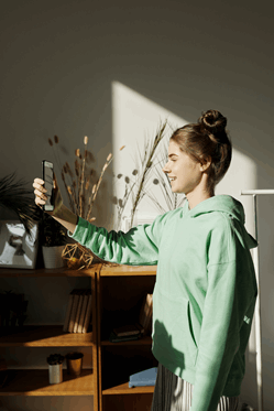 La imagen muestra a una adolescente con sudadera y el pelo recogido que está sujetando el móvil a la altura de su cara para tomarse una foto. 