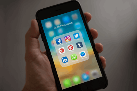  La imagen muestra una mano sosteniendo un teléfono móvil, y en su pantalla se ven los iconos de las nueve redes sociales más conocidas.
