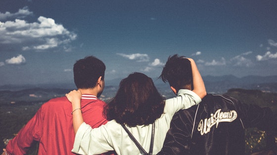 La imagen muestra a tres amigos de espaldas abrazados mirando al horizonte desde una cima.