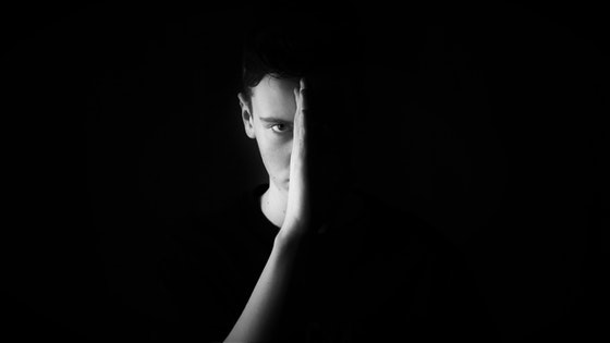 La imagen muestra la cara de un chico iluminada sólo una mitad y la otra oculta por la oscuridad, separando ambas mitades con su propia mano.