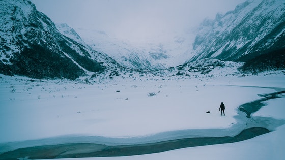 La imagen muestra un paisaje nevado con montañas y de lejos se ve una persona en la nieve.