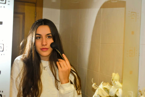 La foto muestra una chica delante de un espejo maquillándose.