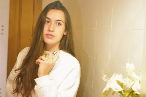 La foto muestra una chica delante de un espejo echándose perfume