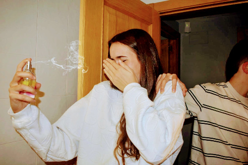 La foto muestra a una chica protegiéndose la cara porque se ha echado perfume en los ojos por error al asustarse cuando le tocan el hombro