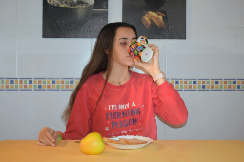 La foto muestra una chica bebiendo café en una cocina y con su desayuno delante.