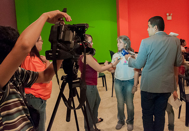 Fotografía de un estudio donde un hombre y una mujer están entrevistando a una niña mientras una cámara de vídeo graba la escena. 