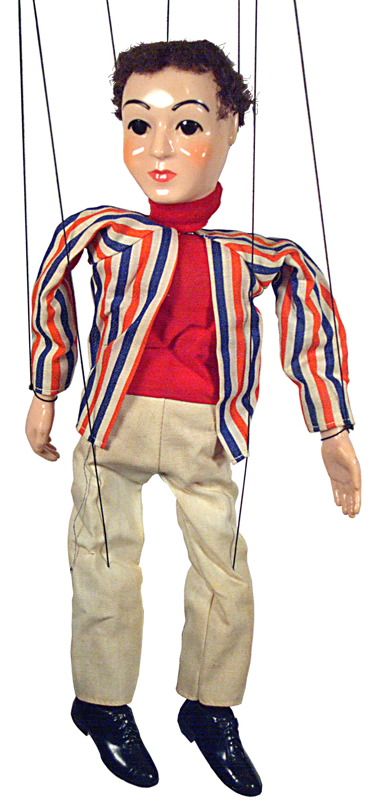 La imagen muestra marioneta de un chico, moreno de pelo corto y ojos oscuros. Vestido con un jersey rojo, pantalón beige y chaqueta de rayas rojas y azules