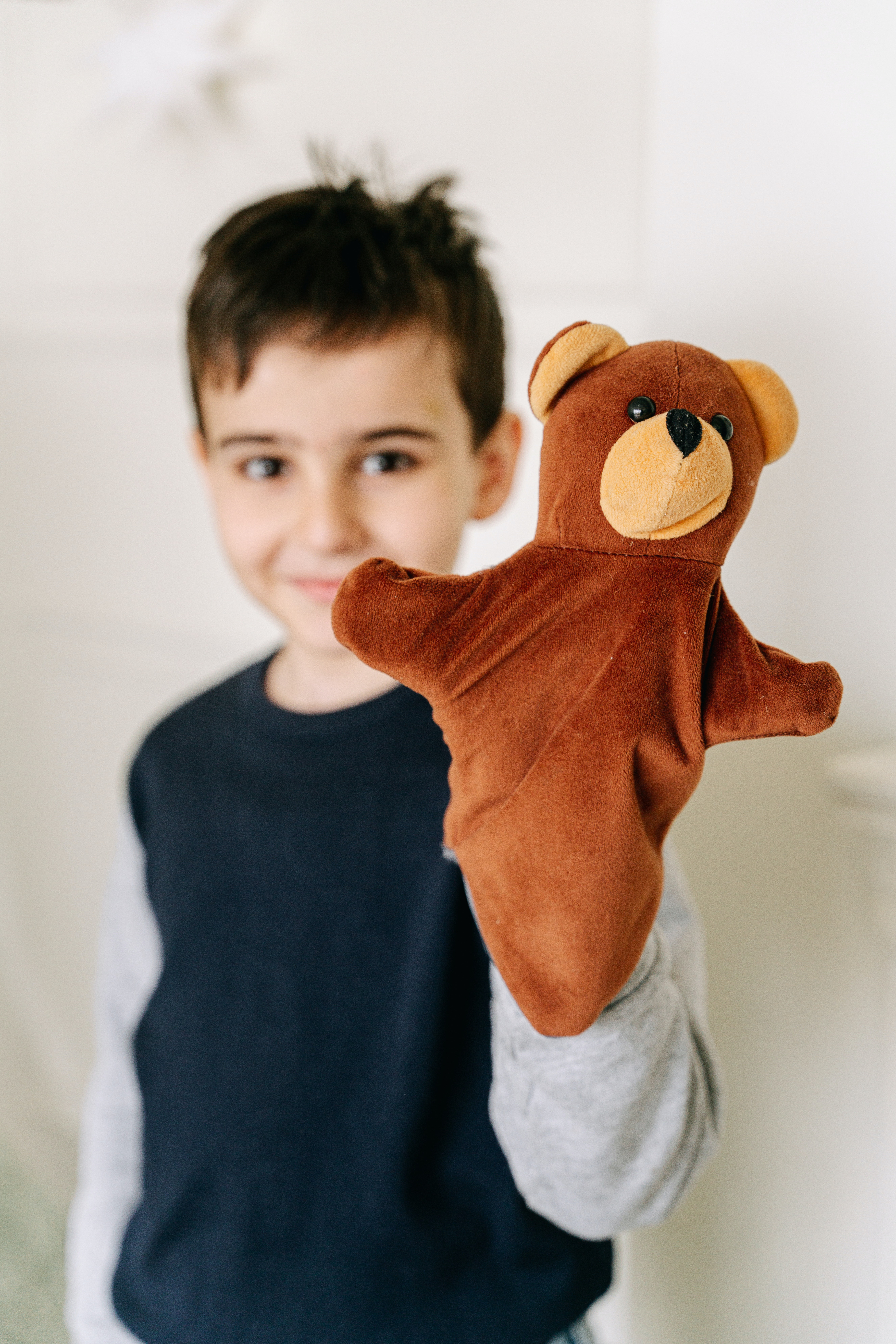 La imagen muestra un niño sonriendo con una marioneta de mano, un osito marrón