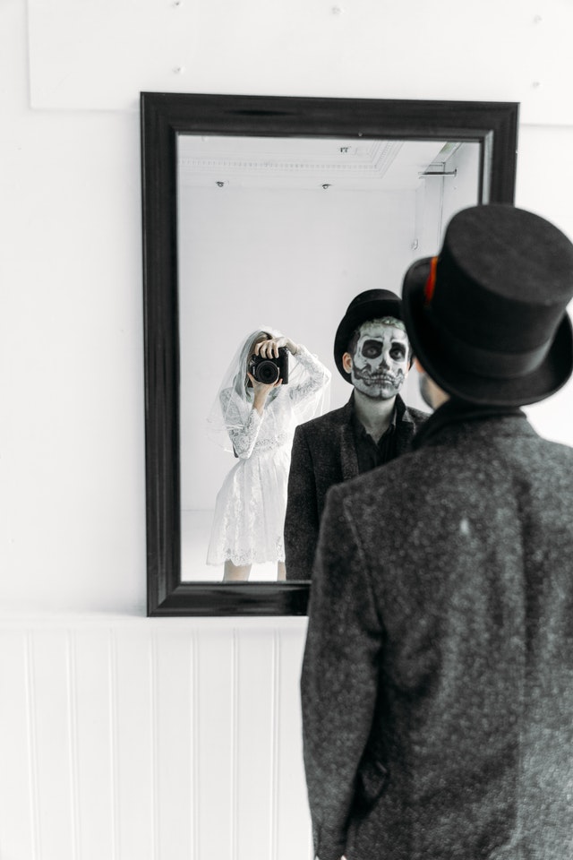 La imagen muestra una chica disfrazada con una cámara y un chico disfrazado ante un espejo