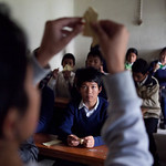 En la imagen puedes ver un chico mostrando cómo se hace una figura de origami ante sus compañeros de clase