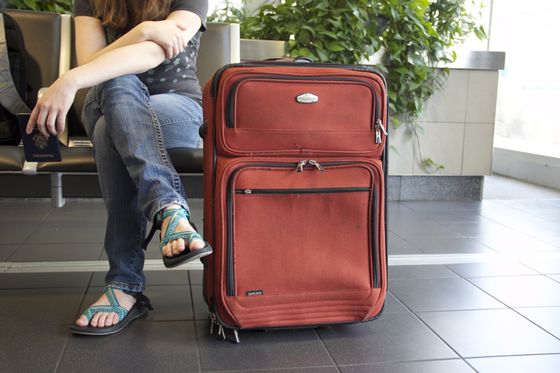 Chica esperando en el aeropuerto con su maleta.