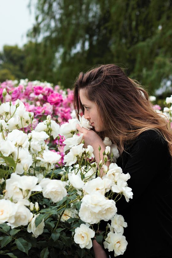 Chica oliendo una flor en un jardín.