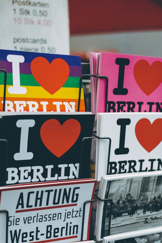 Imagen de postales de Berlín con diferentes dibujos y formatos colocadas en un soporte de metal blanco. En la parte superior están puesto los precios de las diferentes postales.