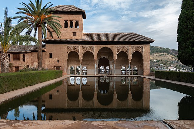 Foto del interior de la Alhambra donde se ve un patio con un estanque y un porche con columnas. 