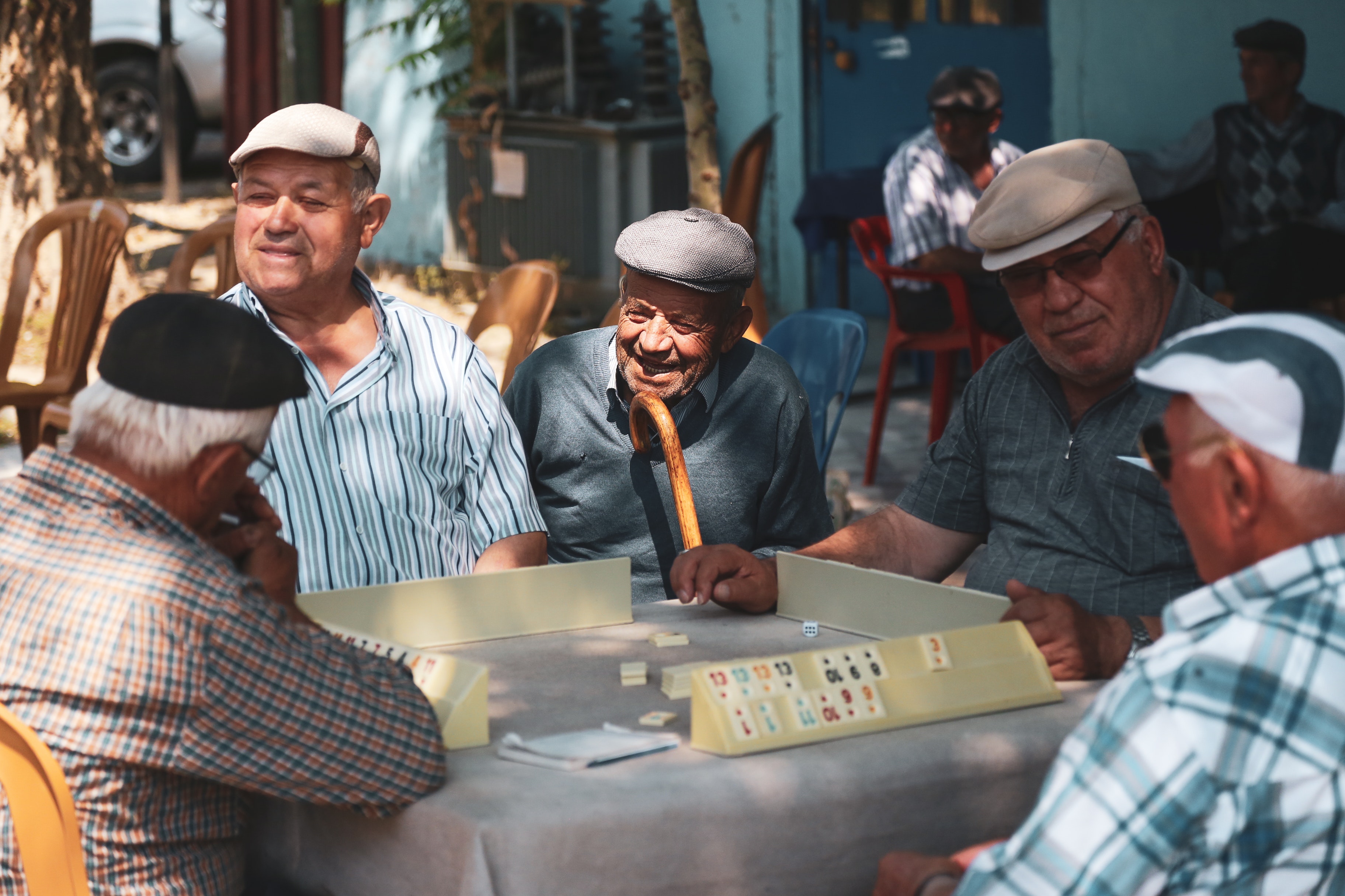 La imagen muestra a cinco señores mayores jugando a un juego de mesa y charlando animadamente. Todos ellos llevan una boina y uno de ellos tiene un bastón.