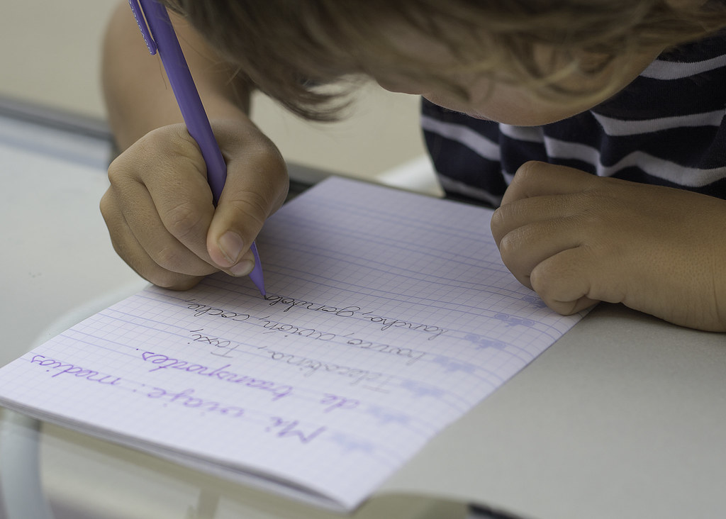 La imagen muestra un  niño escribiendo un texto en un cuaderno.