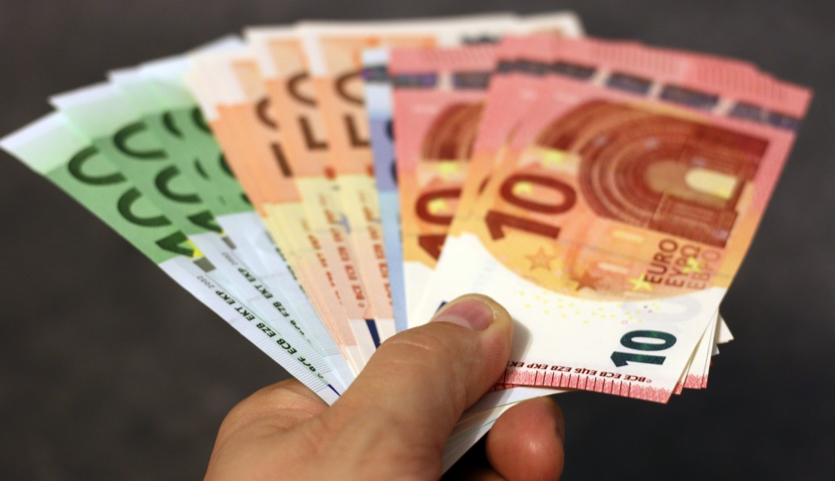 La imagen muestra una mano sujetando varios billetes de euros.