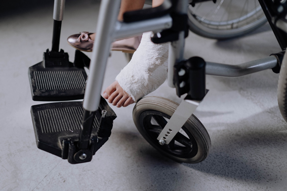 La imagen muestra la parte de abajo de una silla de ruedas y una pierna escayolada.