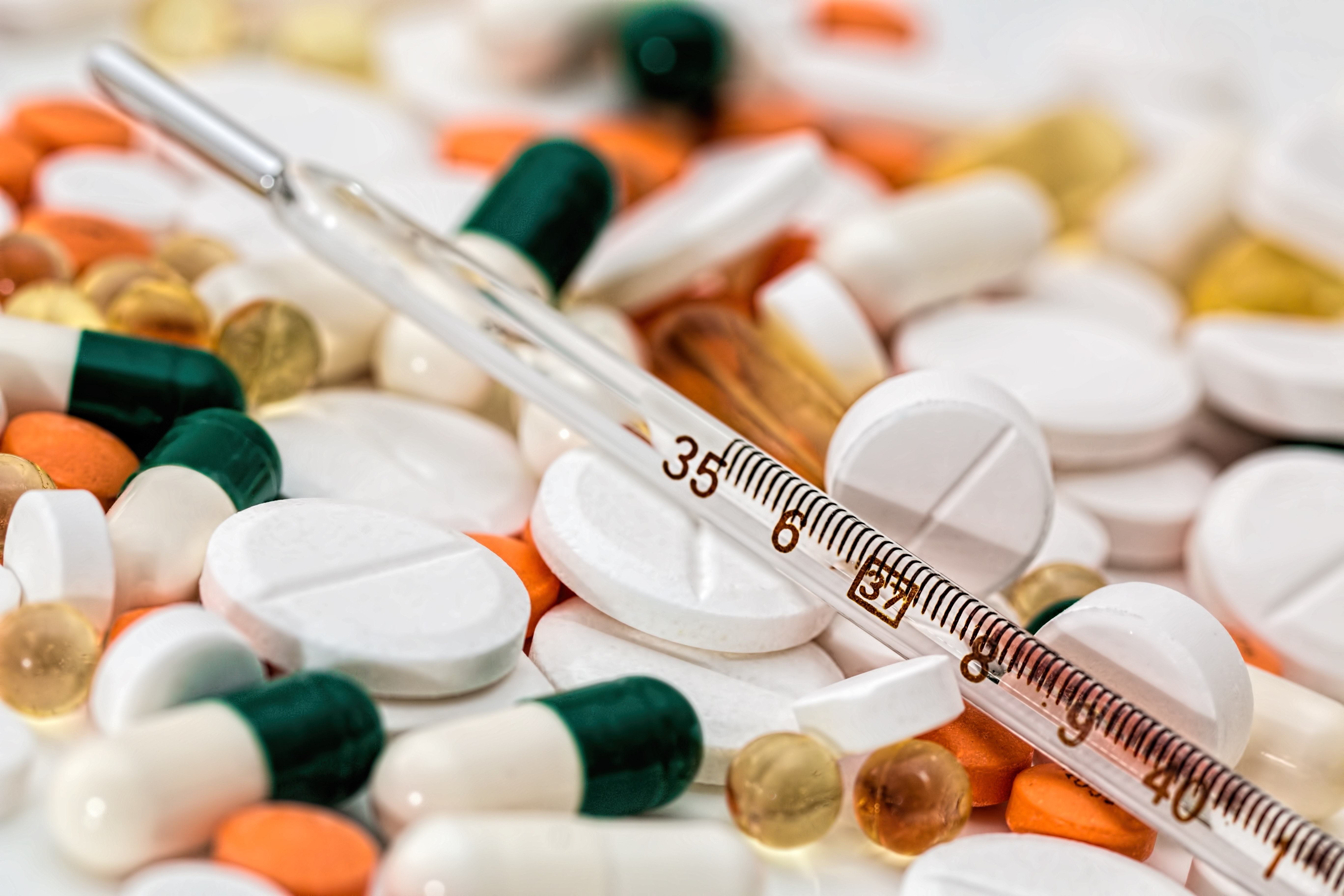 La imagen muestra una colección de medicamentos y un termómetro médico.