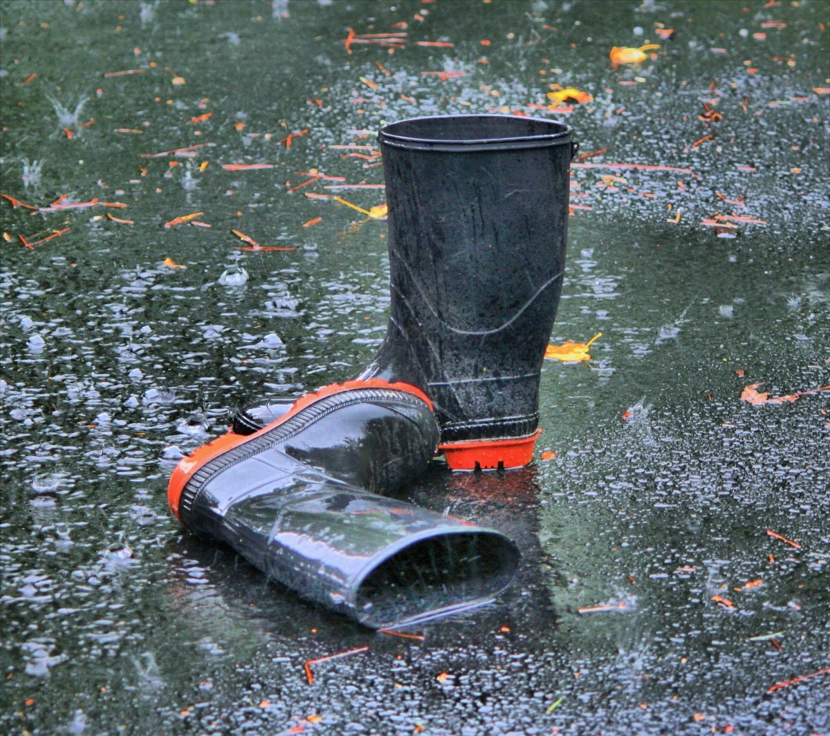 La imagen muestra unas botas impermeables en una calle bajo el agua de la lluvia. 