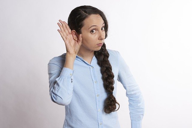 Una chica con la mano amplificando su oreja muestra interés por escuchar.