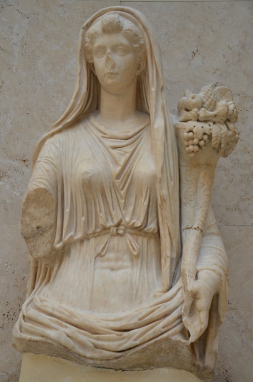 statua sedente de la emperatriz Livia. como Fortuna o Abundancia. Vestida con túnica y manto que le cubre la cabeza, porta en su brazo una cornucopia, símbolo de la abundancia