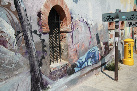 La imagen muestra un grafiti sobre un muro de Granada que representa un hombre acostado bajo una ventana con arco de herradura y un buzón de correos al fondo.
