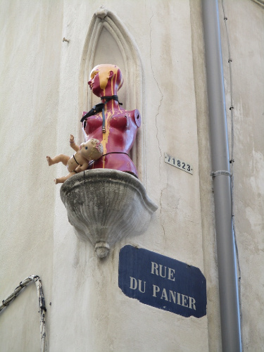 La imagen muestra el busto de un maniquí y un muñeco sobre una peana de una fachada de una calle.