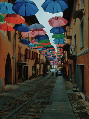 La imagen muestra una calle cubierta de sombrillas abiertas de muchos colores.