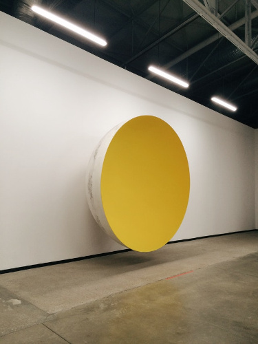 La imagen muestra un cuenco gigante de color amarillo sobre una pared.